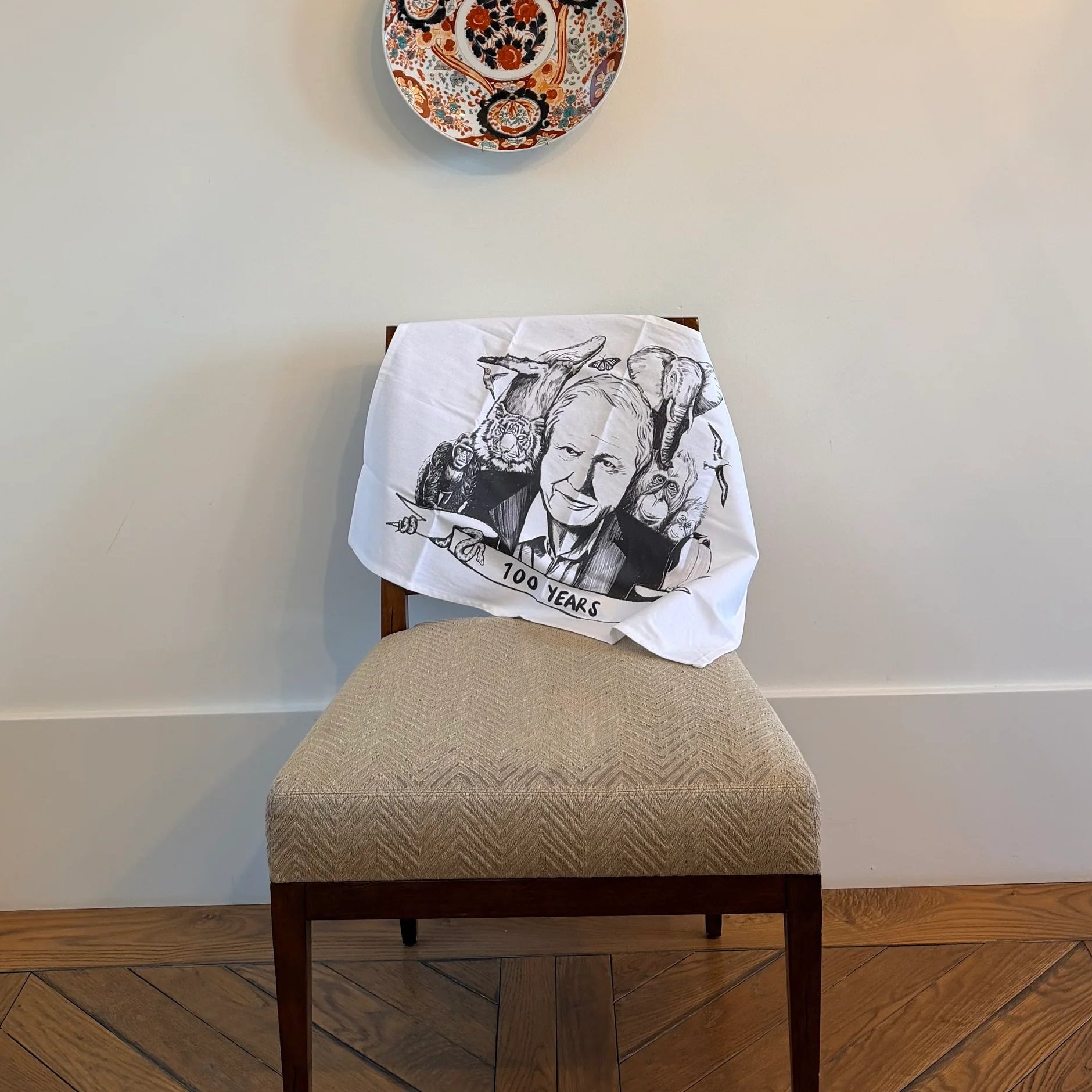 Chair with a white towel featuring a black and white design, against a wall with three decorative plates.