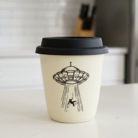 White ceramic cup with black lid featuring a UFO design on a white background