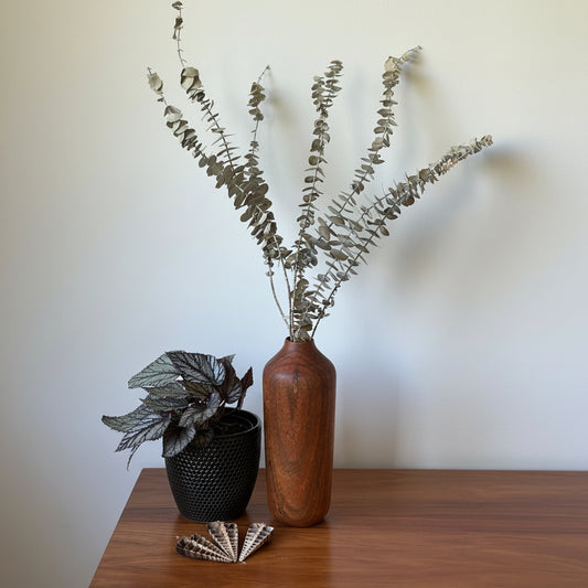 Decorative arrangement with a wooden vase, black pot, and dried plants on a wooden surface.