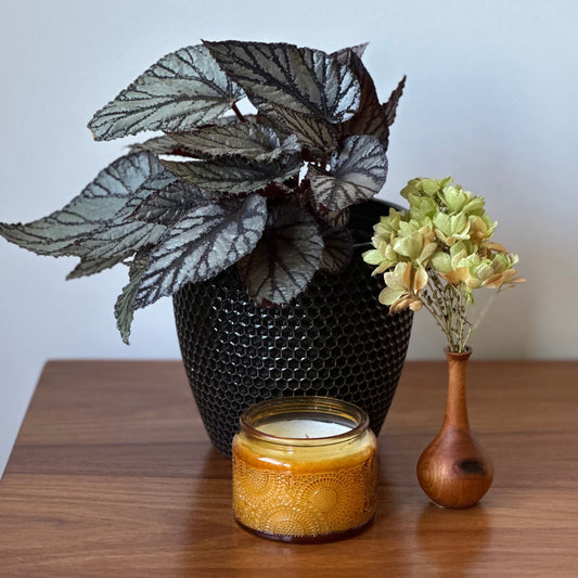 Decorative items including a black textured vase with a plant, a yellow candle in a glass holder, and a small wooden vase with flowers on a wooden surface.