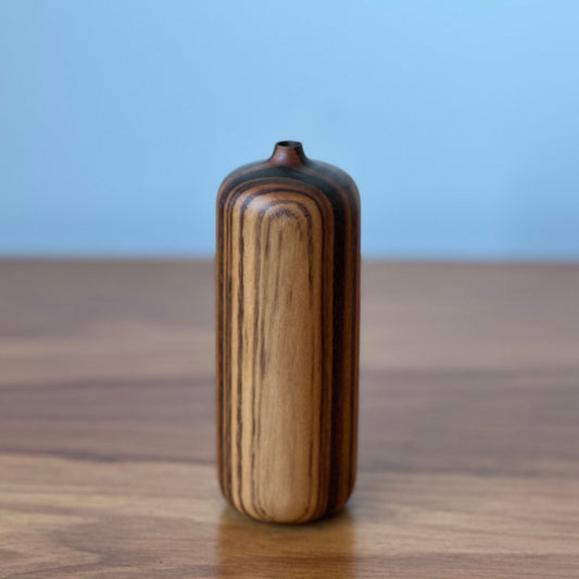Wooden vase with striped pattern on a wooden surface with a blue background