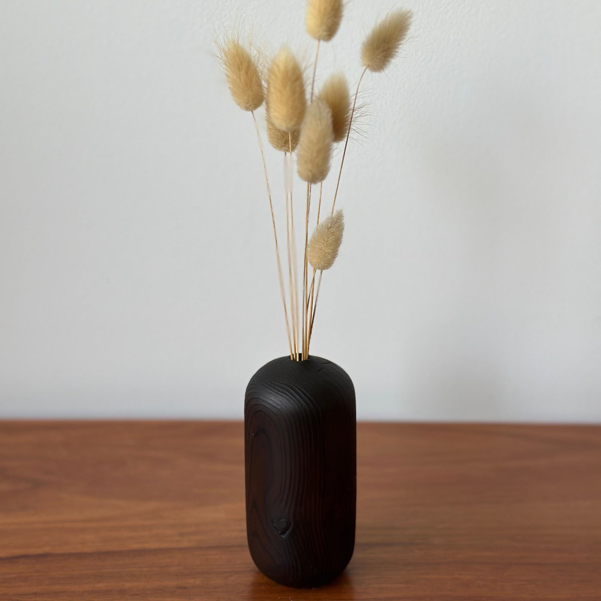 Huon vase with dried grasses on a wooden surface against a white wall