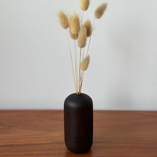 Huon vase with dried grasses on a wooden surface against a white wall