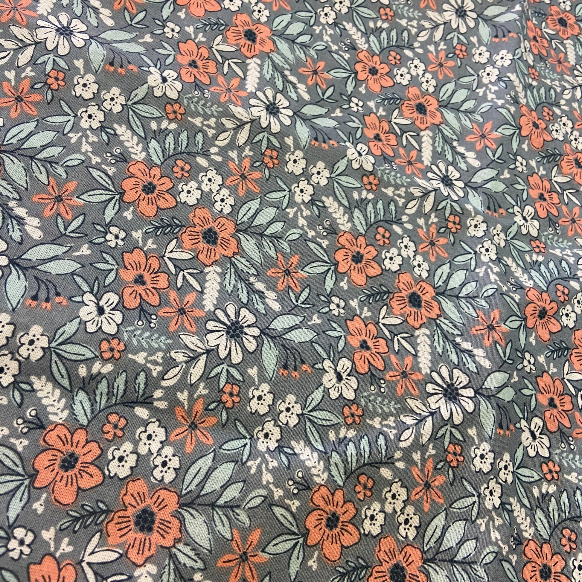 A close-up of a floral fabric pattern featuring orange, white, and light blue flowers with green leaves on a muted gray background.