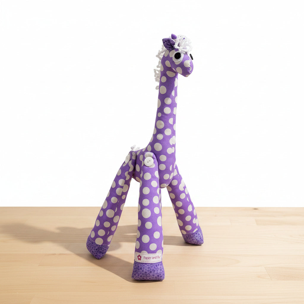 A purple and white polka dot plush giraffe toy standing on a dark gray tiled floor against a matching tiled wall.