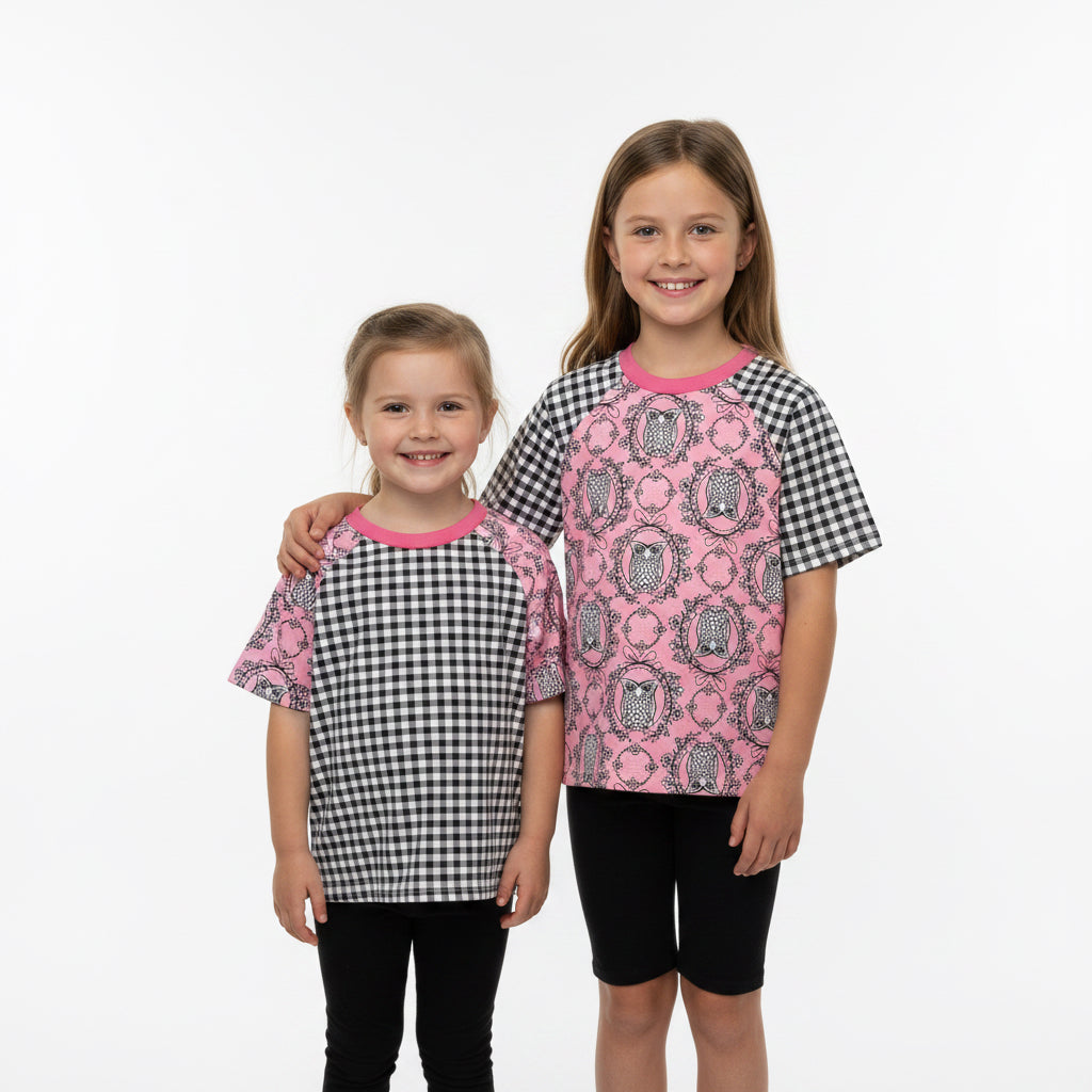Two children's shirts with pink and black patterns on a wooden floor.