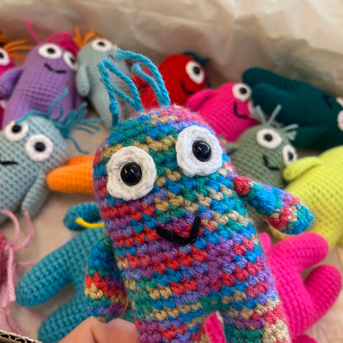 Colorful crochet monsters with various patterns and colors on a textured surface.