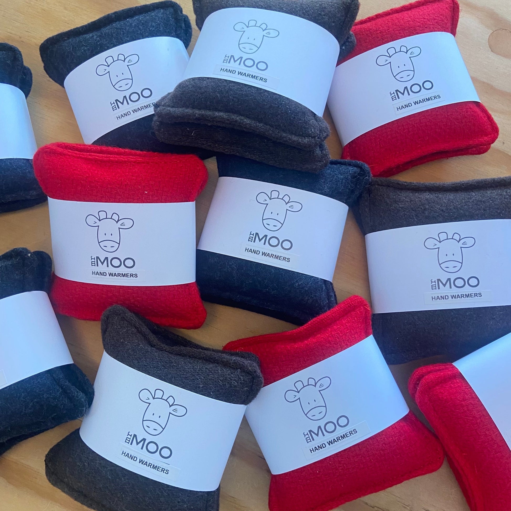 Hand warmers in black, red, and gray with MR MOO branding on a wooden surface.