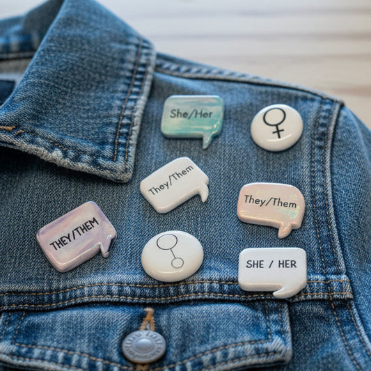 Denim jacket with various pronoun pins on a blurred background
