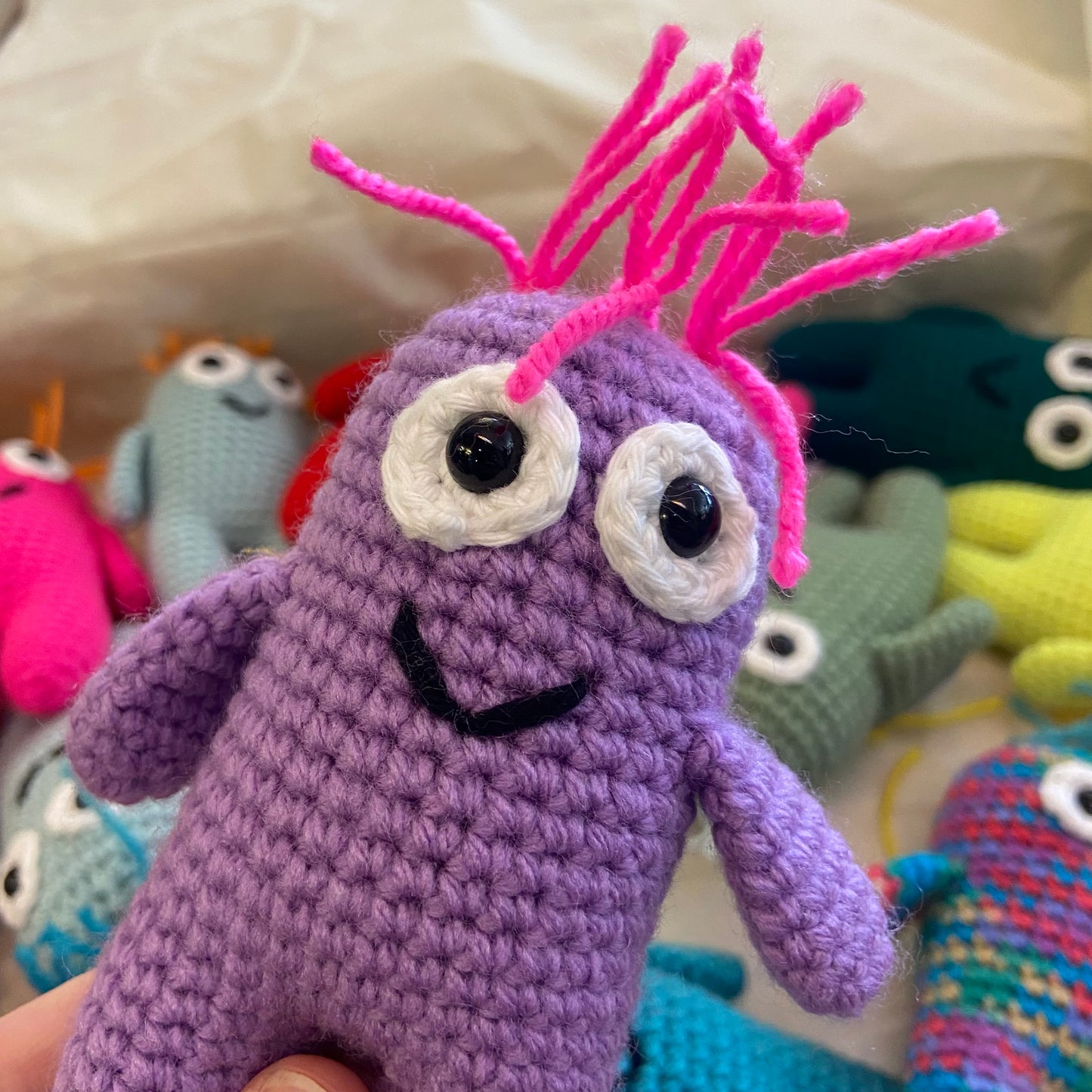 Purple crochet creature with pink hair among other colorful creatures.