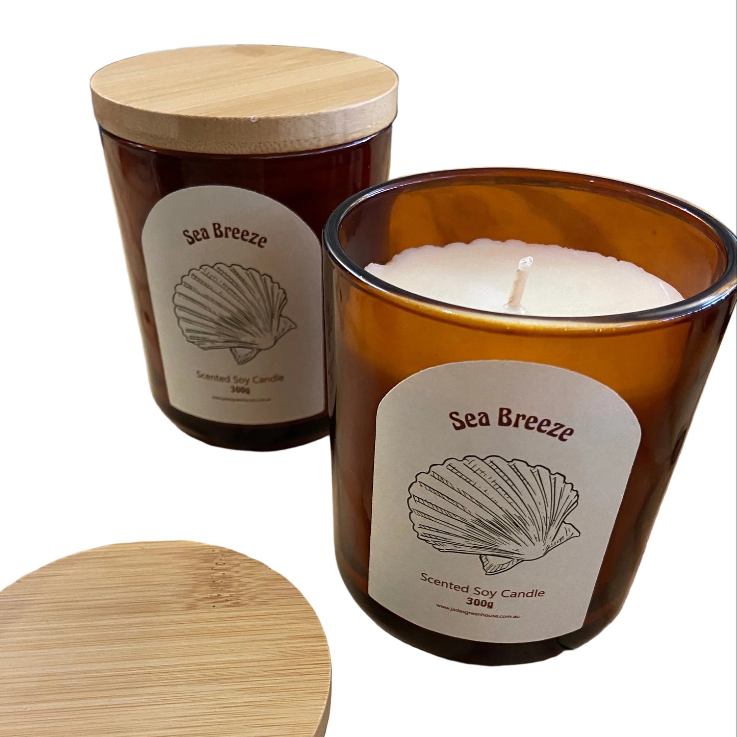Two amber glass scented candles with bamboo lids on a wooden table, with one candle open showing white wax and the other standing closed. The labels read 'Sea Breeze'.